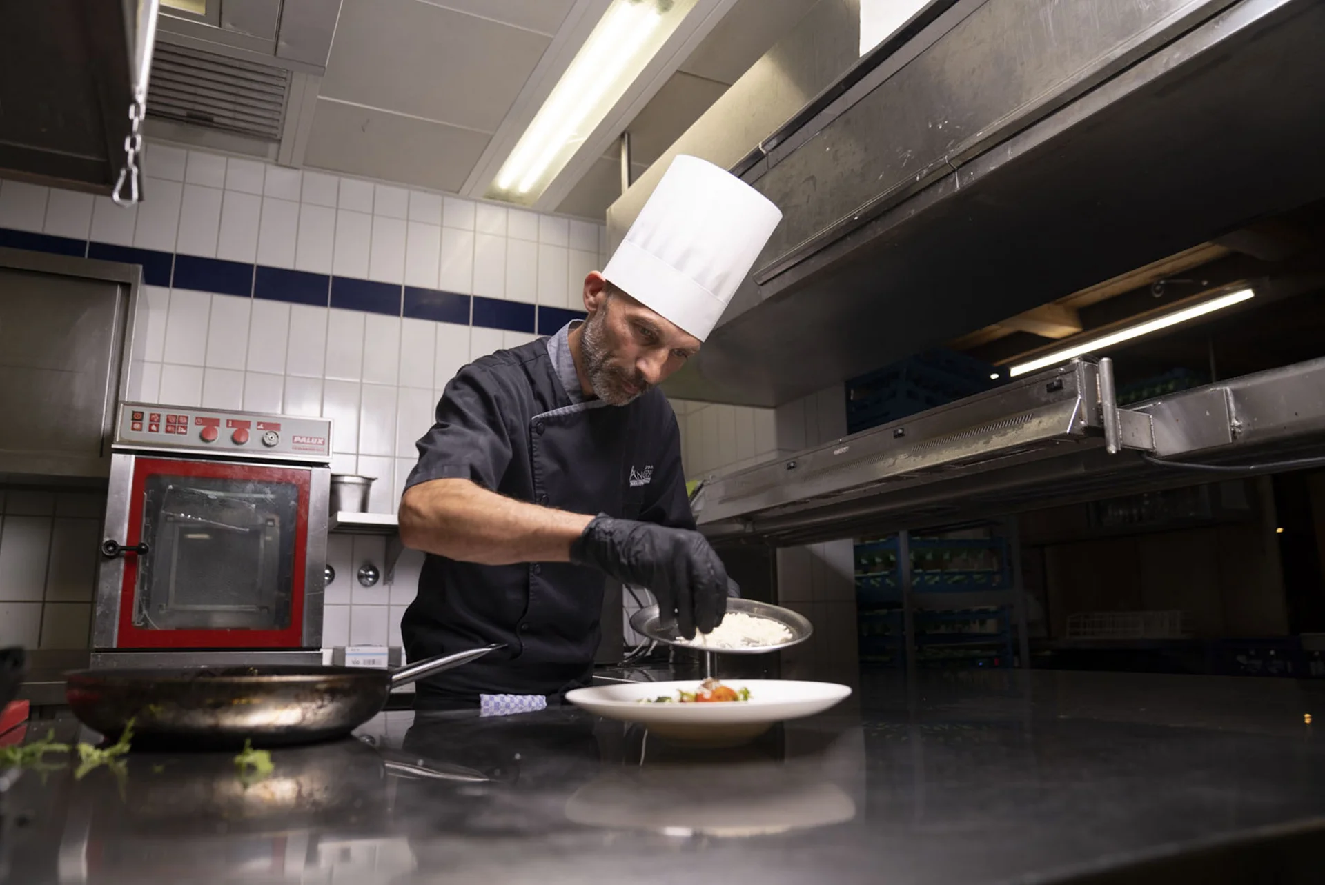 Koch im weißen Hut garniert Gericht in professioneller Restaurantküche