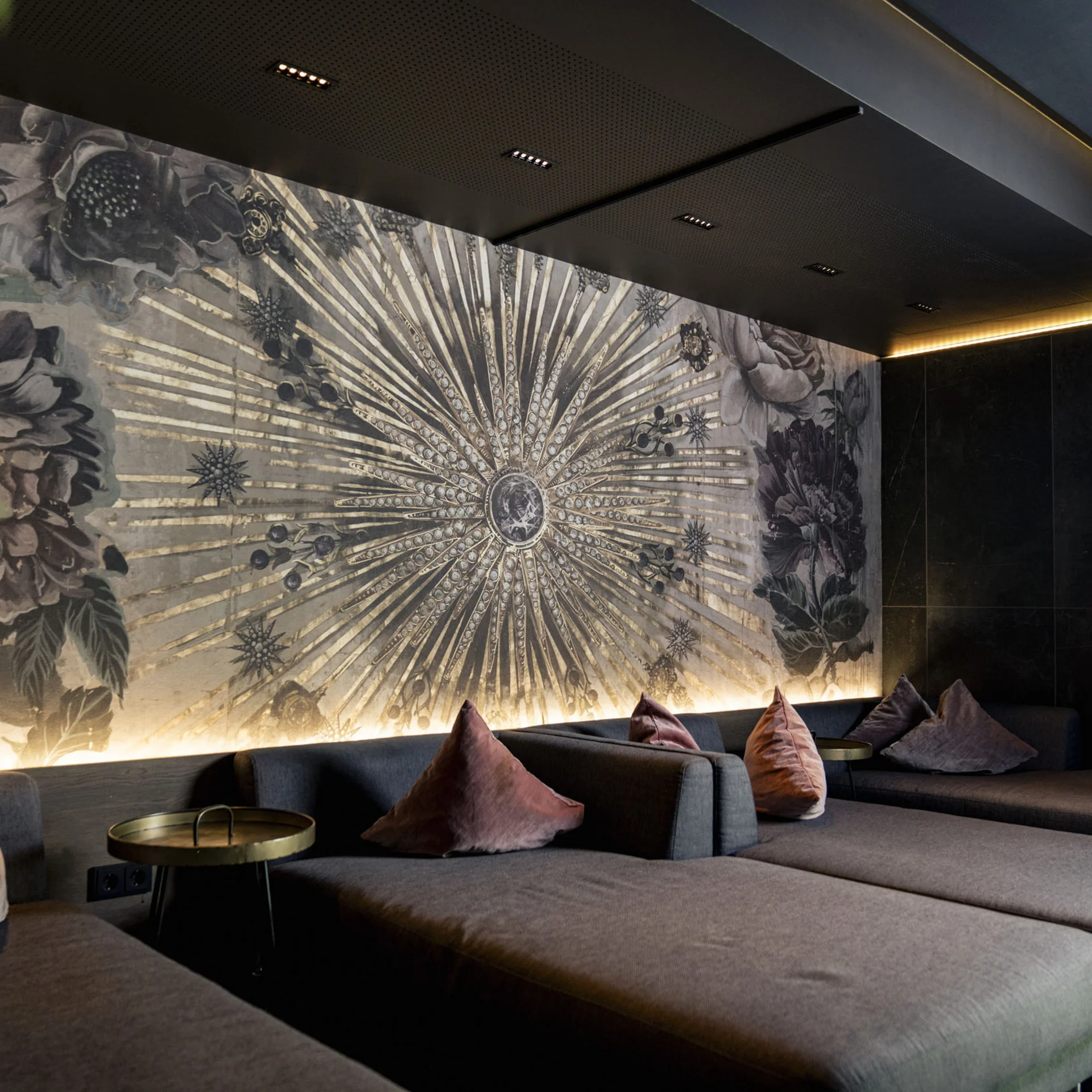Moderne Lounge mit grauen Sofas, bunten Kissen und künstlerischer Wandgestaltung