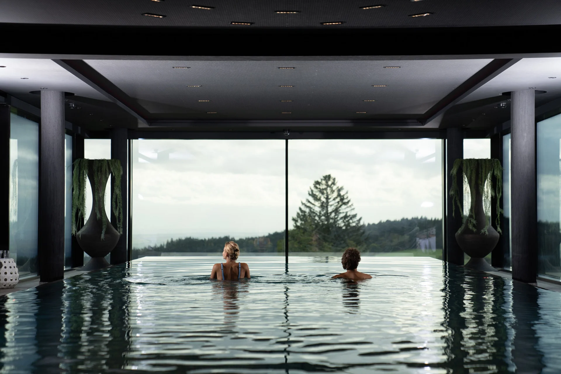 Zwei Personen entspannen im Innenpool mit Panoramablick auf Wald und Berge