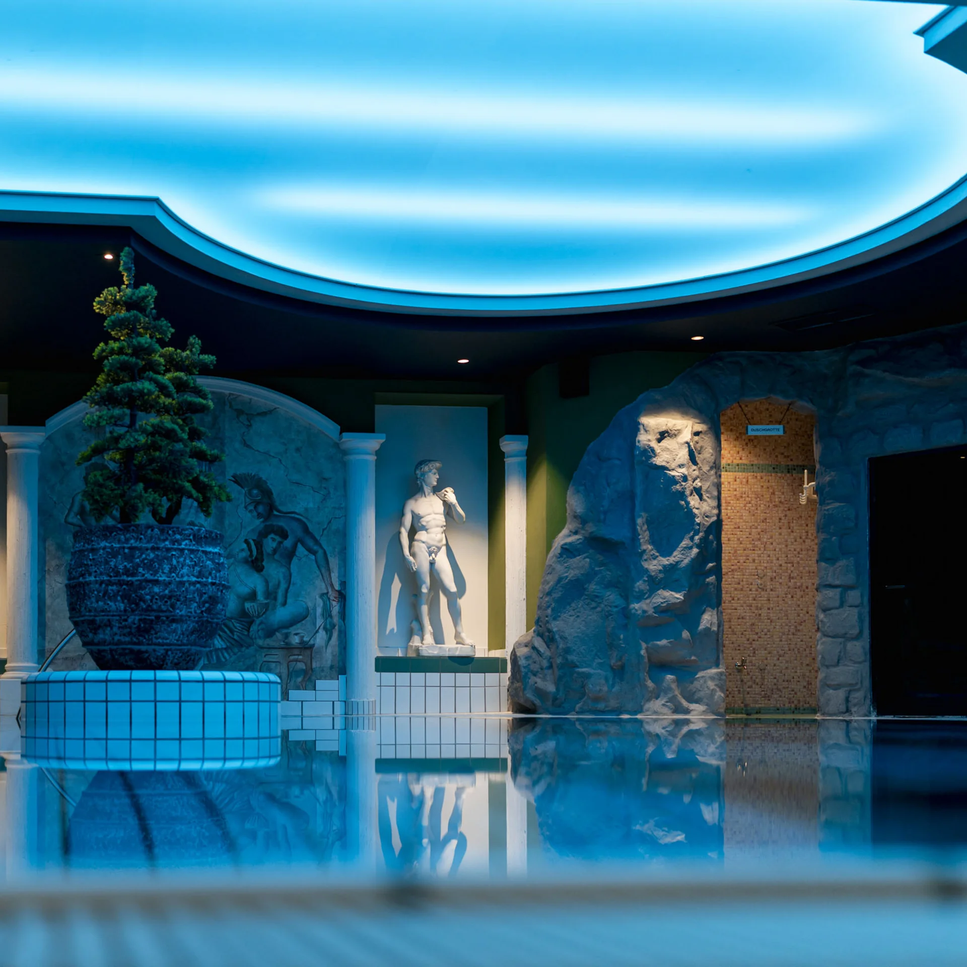 Innenpool mit antiken Statuen und blau beleuchtetem Gewölbedeckenlicht