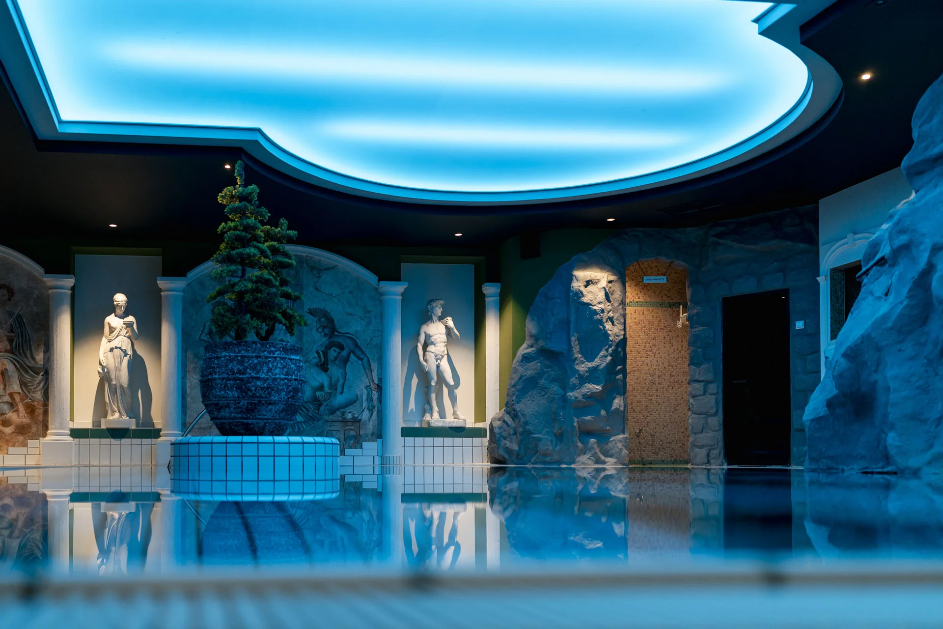 Innenpool mit antiken Statuen und blau beleuchtetem Gewölbedeckenlicht