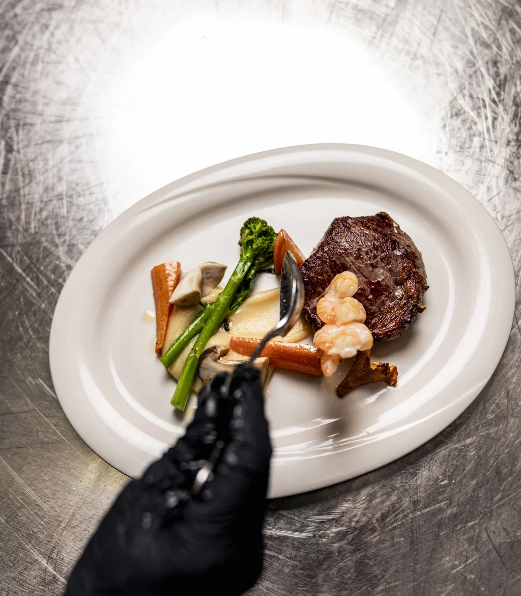 Gehobeltes Gericht mit Steak, Garnelen und Gemüse auf weißem Teller