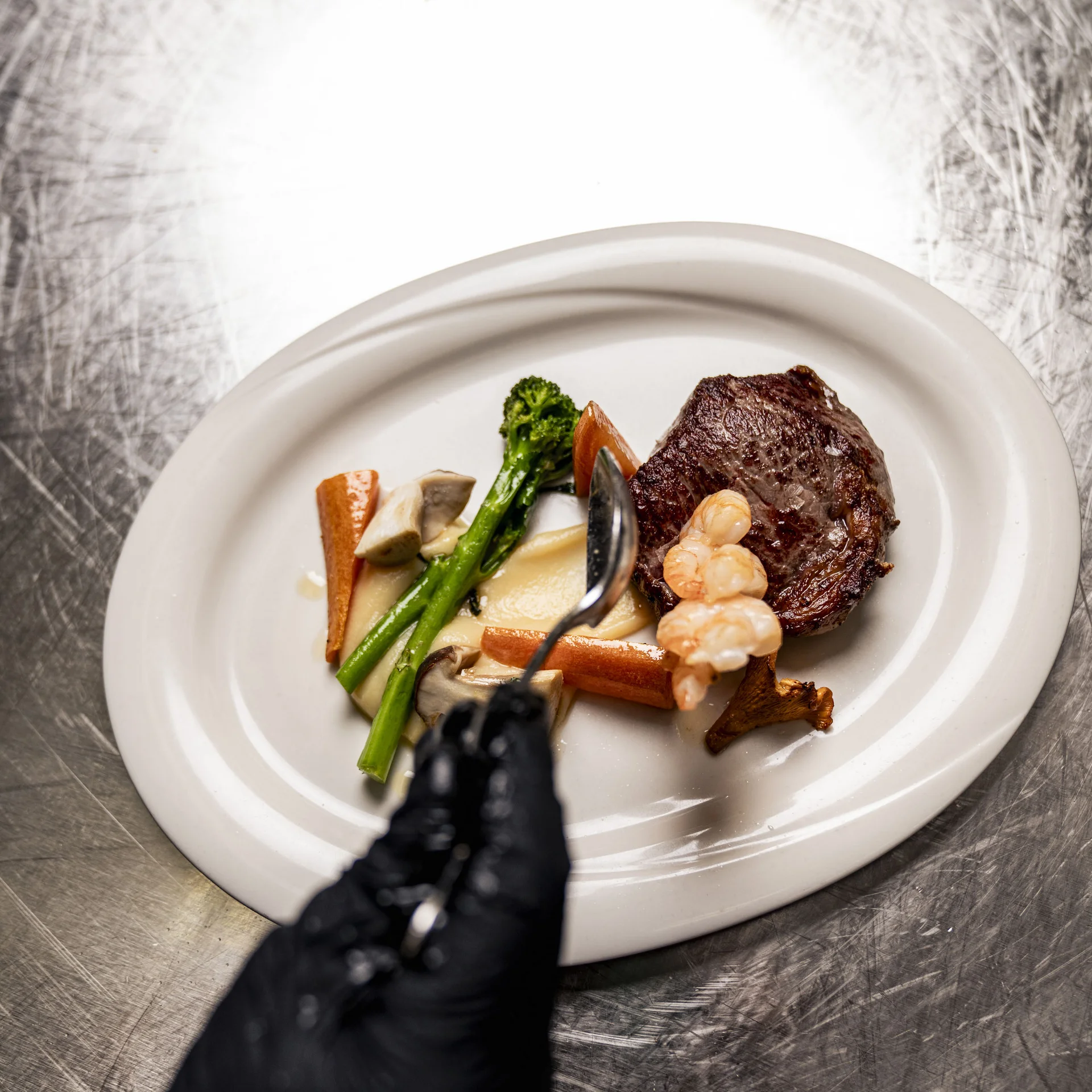 Gehobeltes Gericht mit Steak, Garnelen und Gemüse auf weißem Teller
