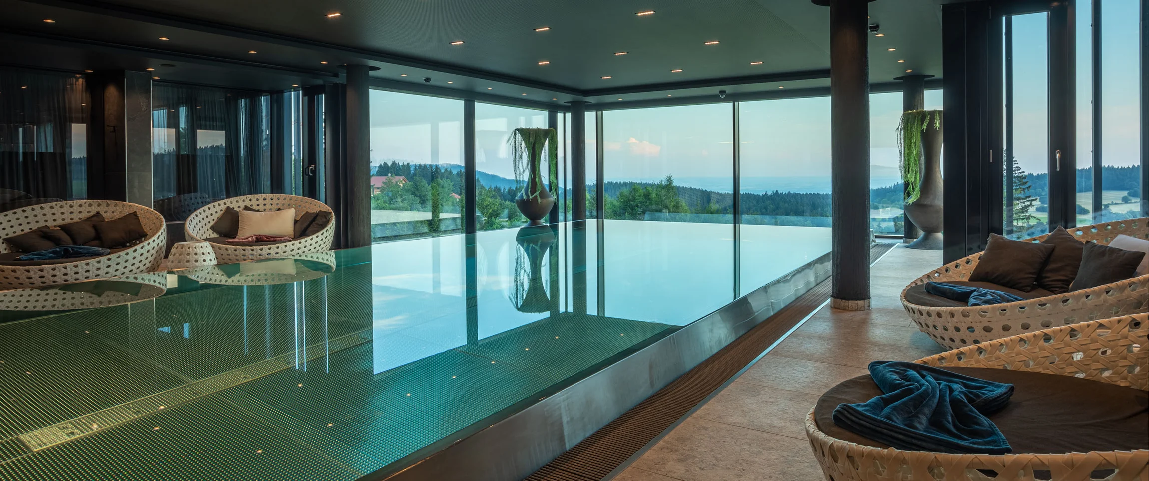 Moderner Innenpool mit Panoramafenstern und Sitzbereich mit Korbstühlen