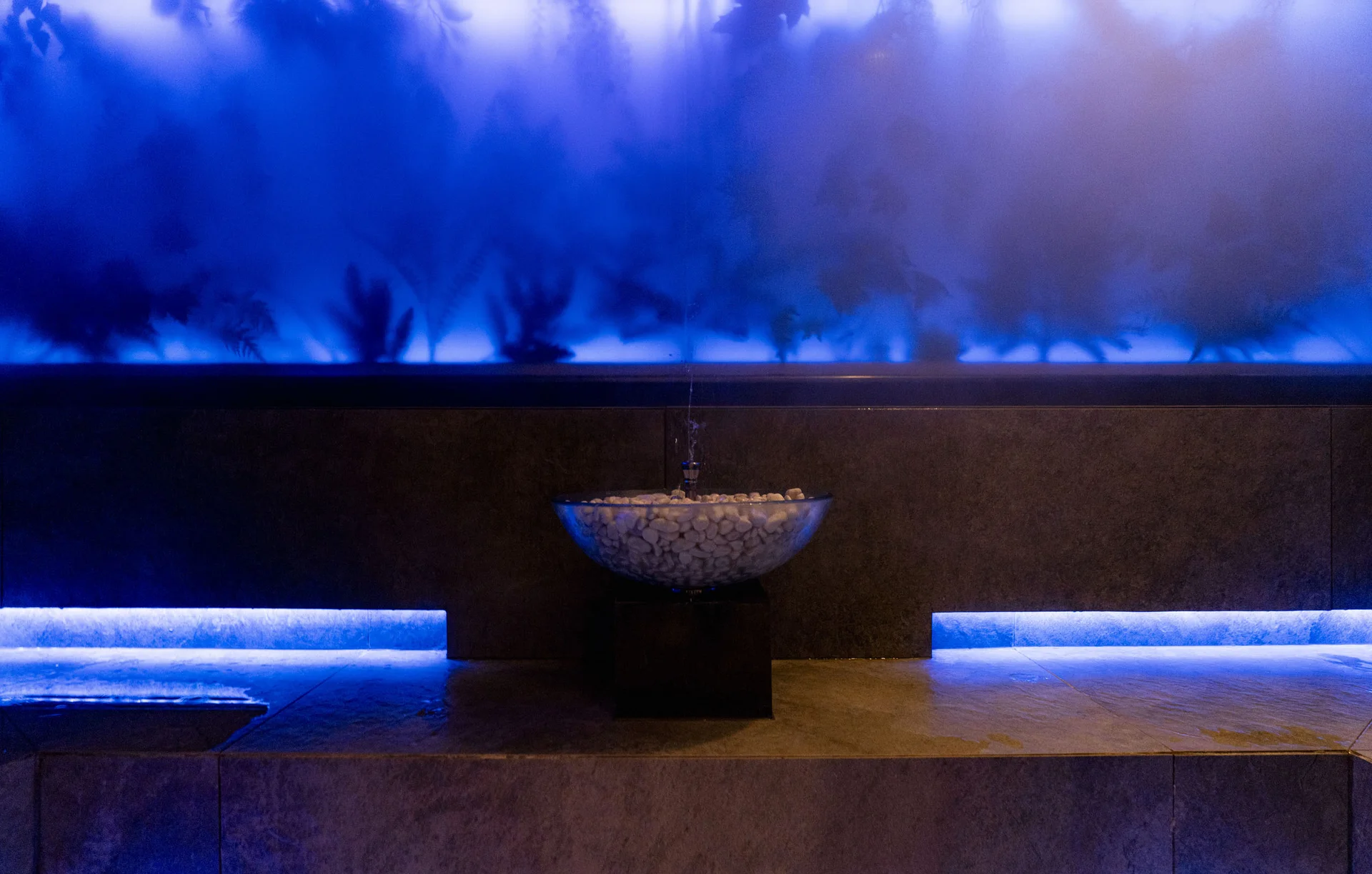 Beleuchteter blauer Raum mit Wasserbecken und Dampfwand