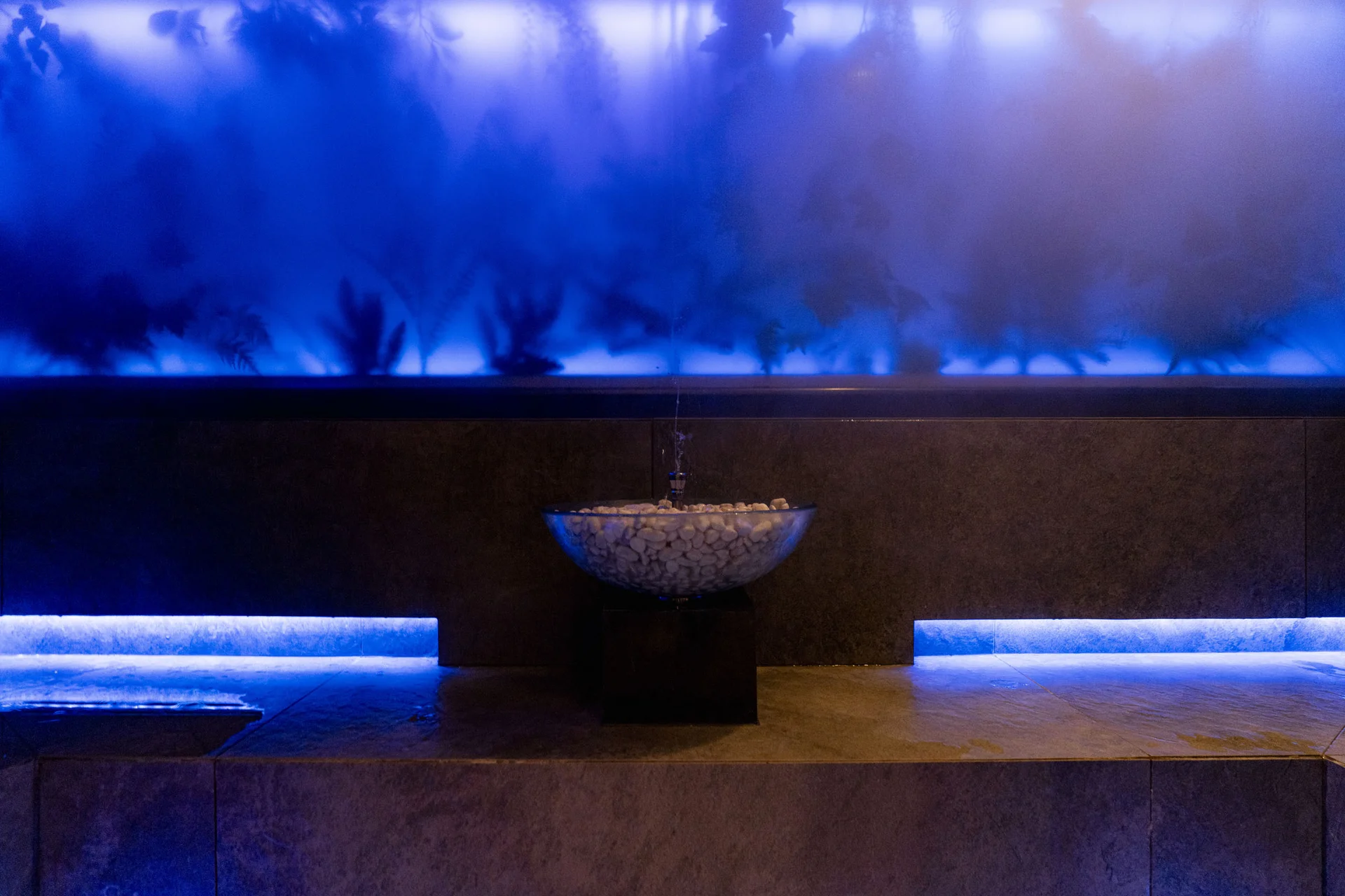 Beleuchteter blauer Raum mit Wasserbecken und Dampfwand