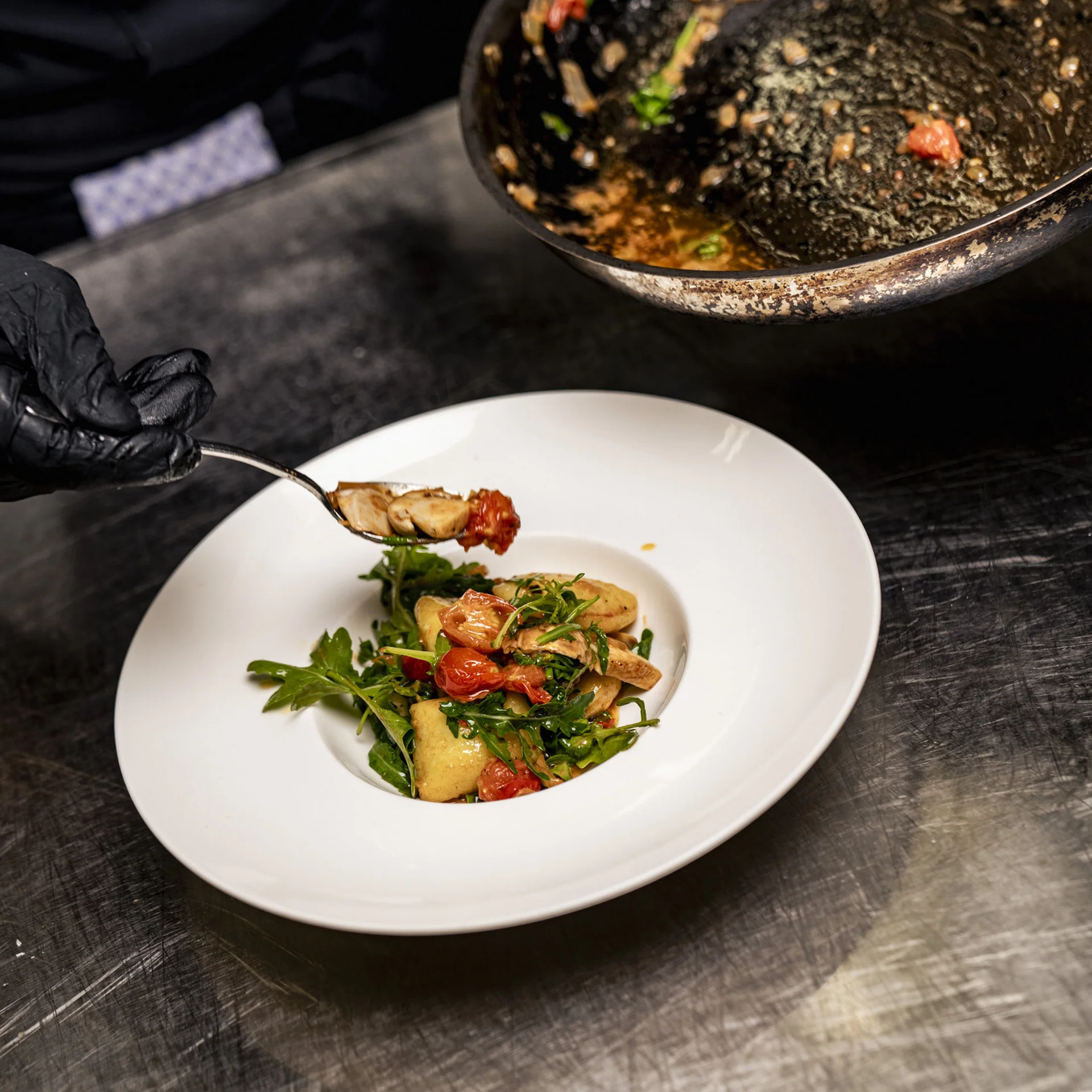 Koch serviert gebratenes Gemüse mit Rucola und Tomaten auf weißem Teller