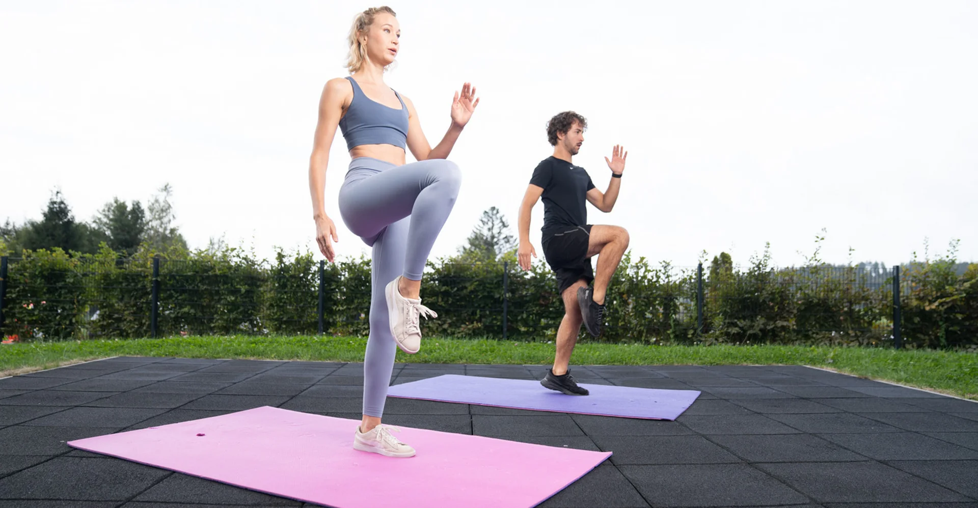 Frau und Mann machen Outdoor-Workout auf Yogamatten im Stehen