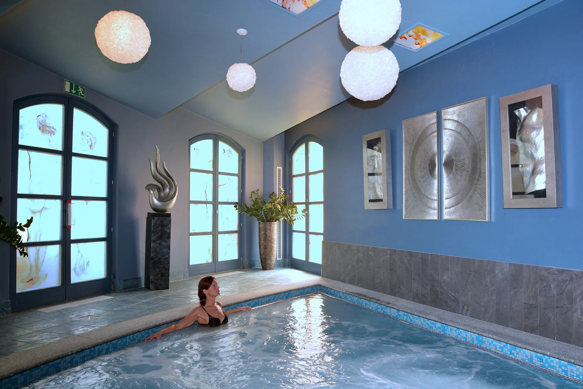Frau entspannt im Hallenbad mit Kunst und Pflanzen