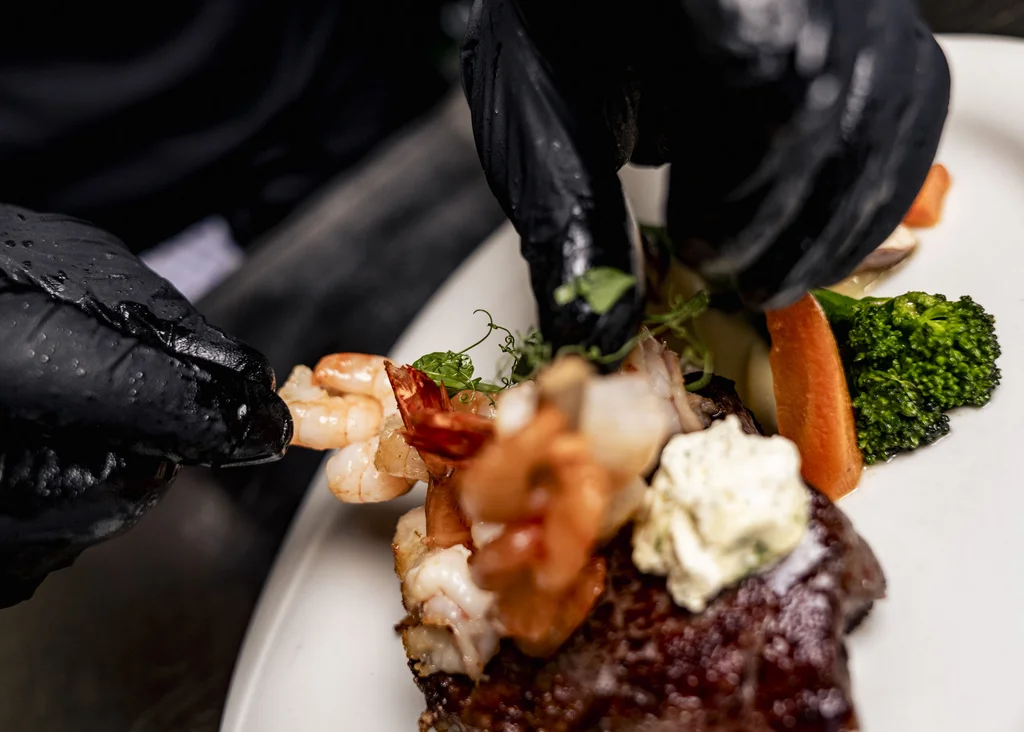 Chef legt mit Handschuhen Garnele auf Steak mit Gemüse