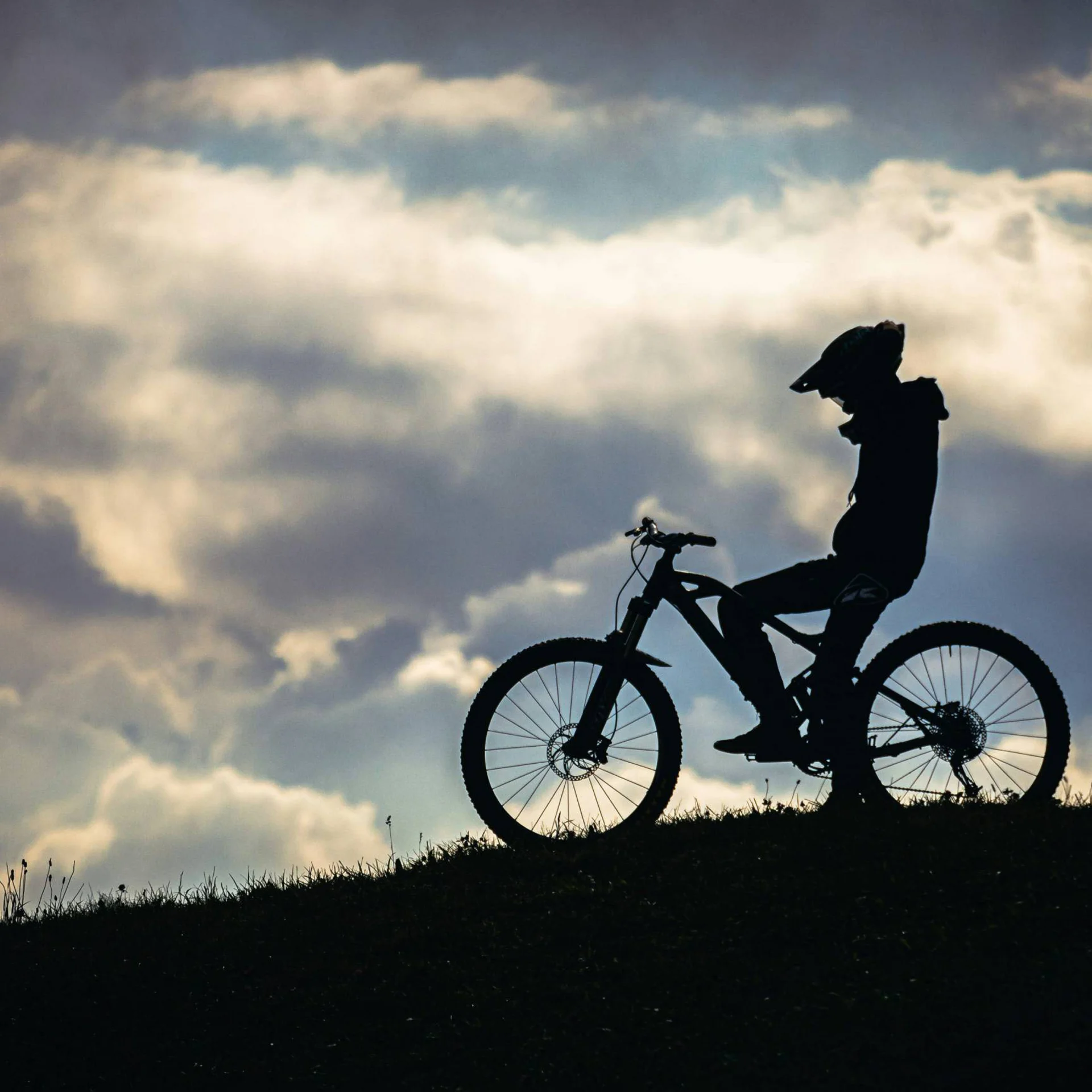 Silhouette eines Fahrradfahrers auf Hügel vor bewölktem Himmel