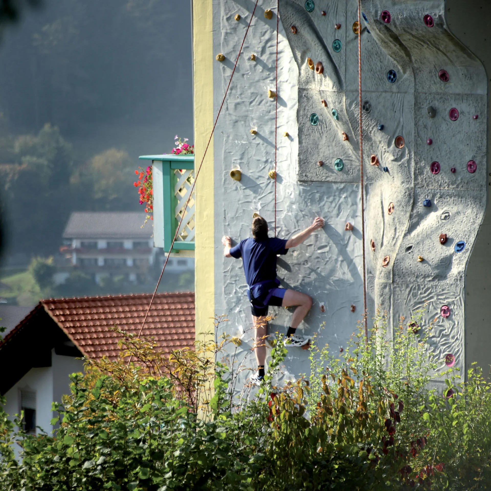 Person klettert auf einer künstlichen Kletterwand an einem Haus im Freien