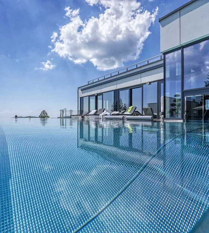 Die Adresse für Wellness in Bayern: Ihr Hotel in St. Englmar Infinity-Pool an einem modernen Gebäude mit Blick auf den See und den blauen Himmel