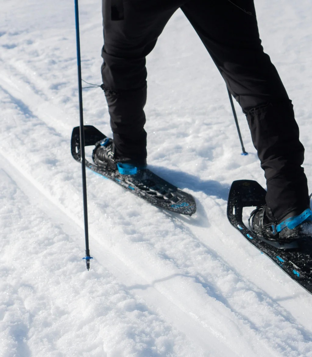 Person läuft mit Schneeschuhen und Stöcken im Schnee
