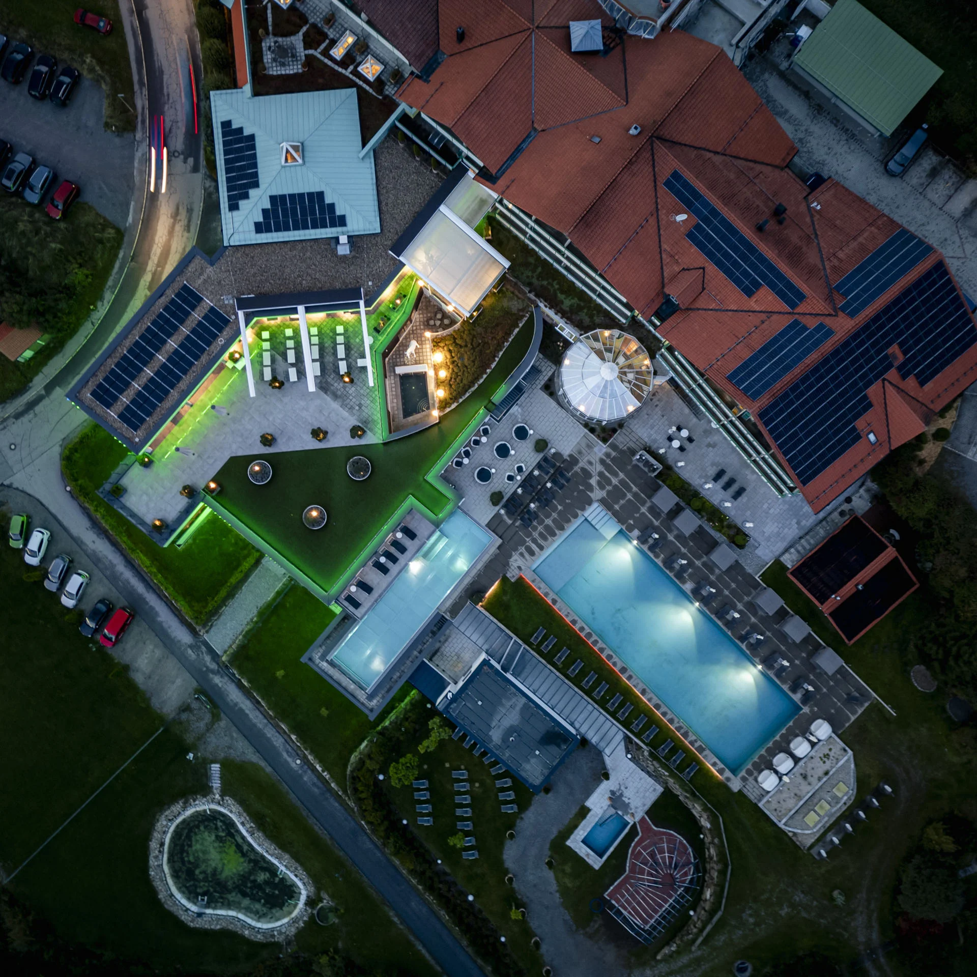 Luftaufnahme eines Hotels mit beleuchtetem Pool und Solarzellen auf dem Dach bei Nacht