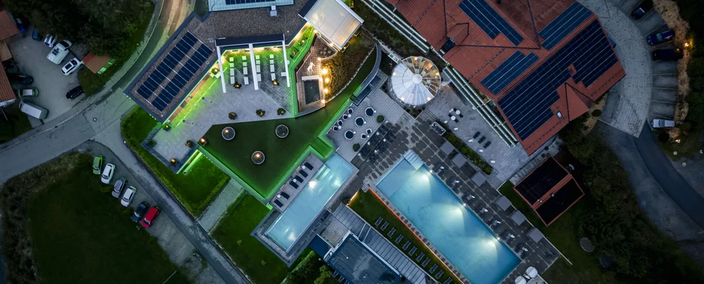 Luftaufnahme eines Hotels mit beleuchtetem Pool und Solarzellen auf dem Dach bei Nacht