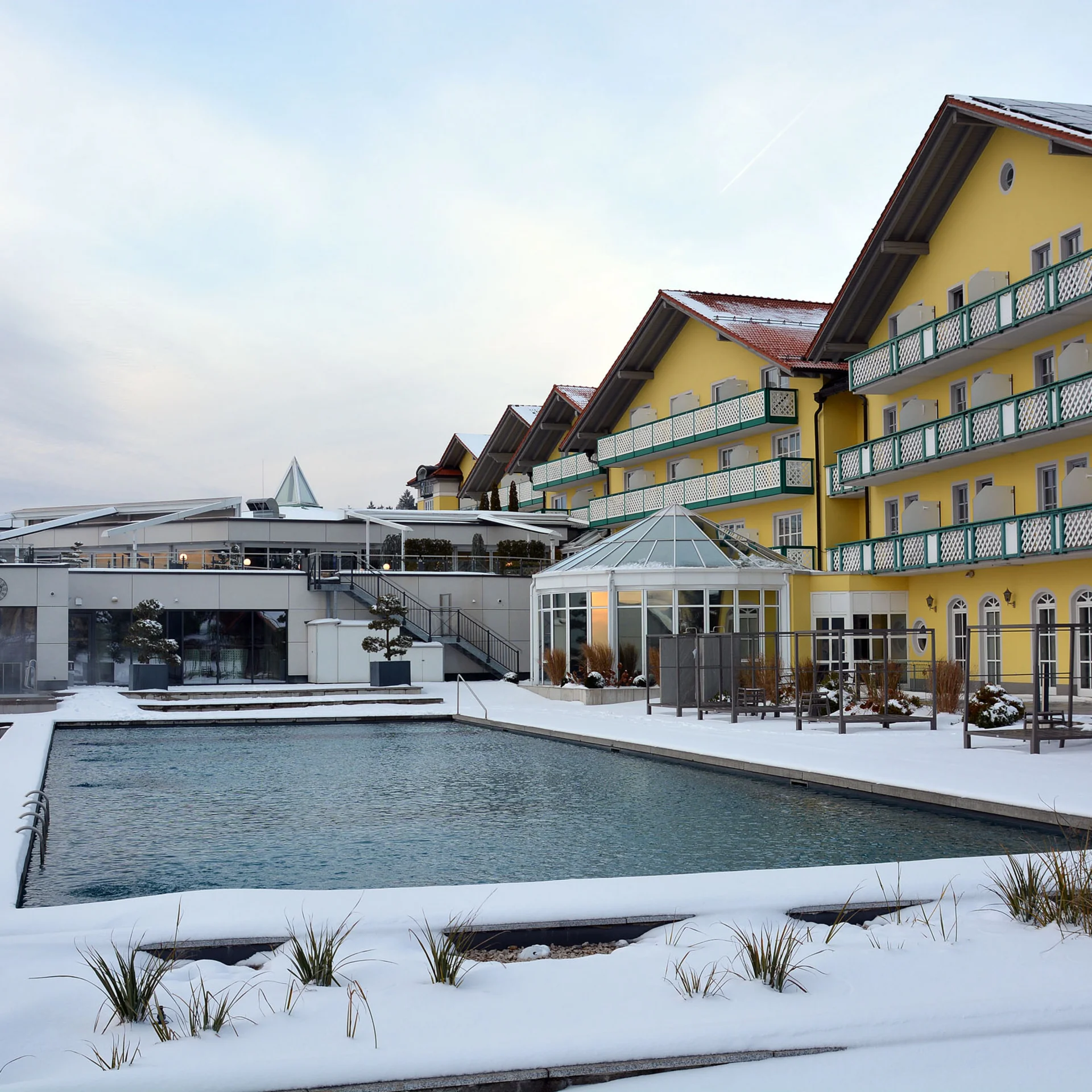 Gelbes Hotelgebäude mit Solarpanelen neben einem Schwimmbecken im Schnee