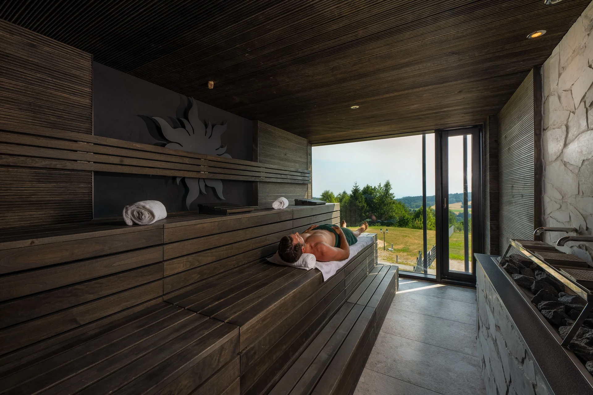 Person entspannt sich in moderner Sauna mit Panoramafenster und Blick ins Grüne
