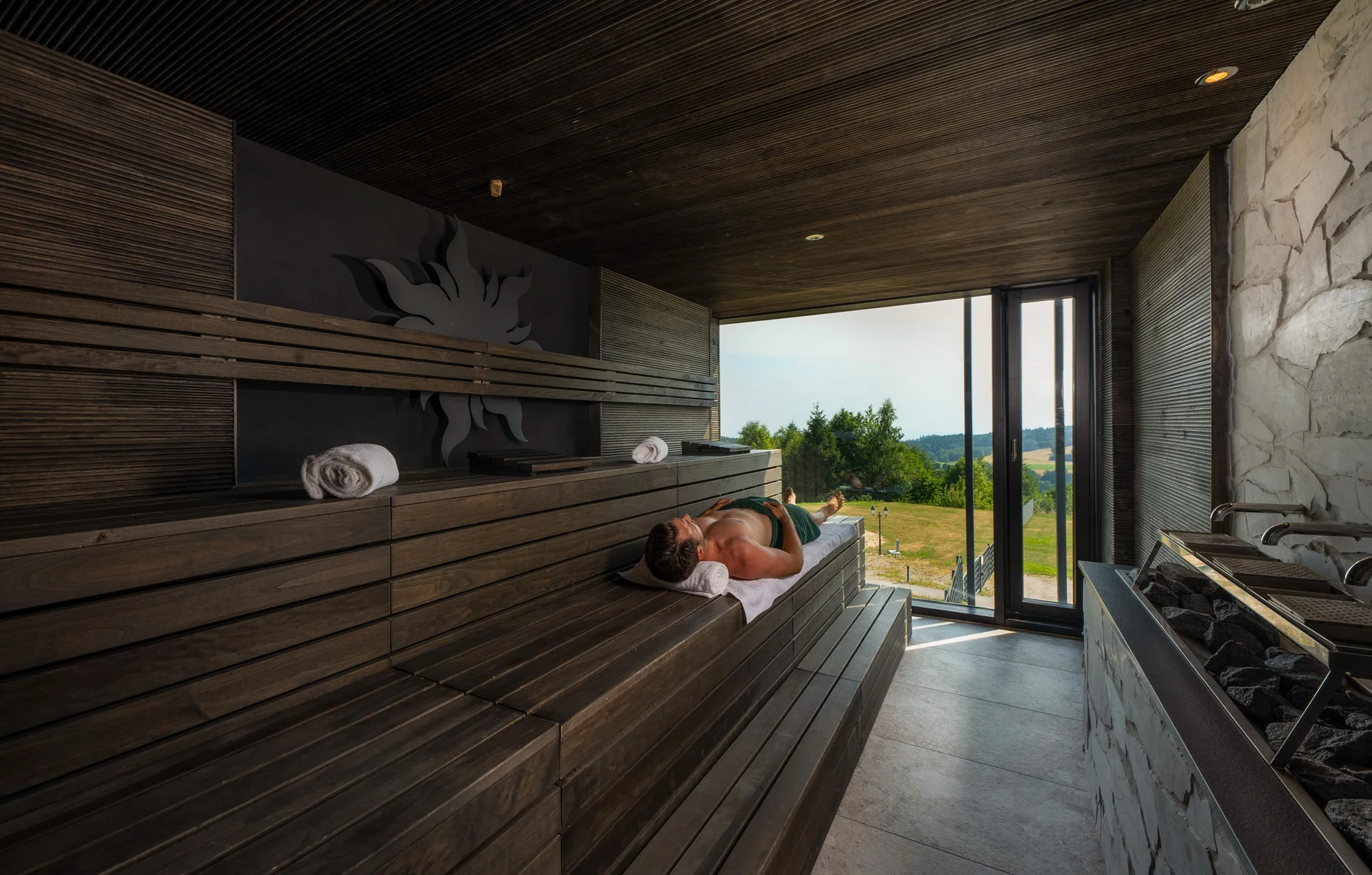 Person entspannt sich in moderner Sauna mit Panoramafenster und Blick ins Grüne