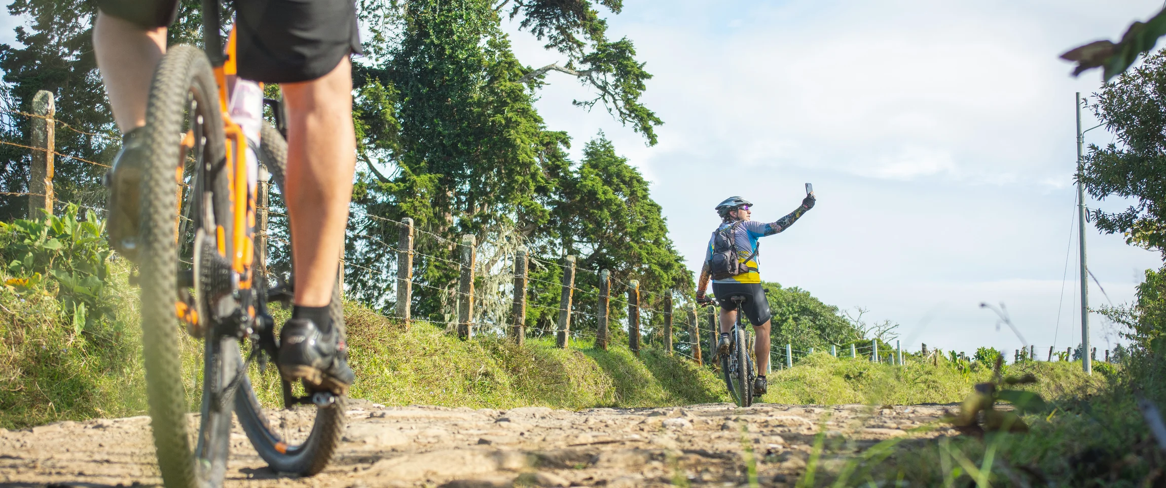 Zwei Radfahrer auf einem Landweg mit Bäumen und blauem Himmel im Hintergrund