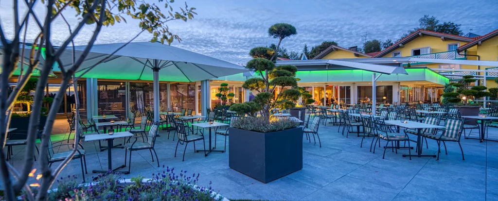 Die Adresse für Wellness in Bayern: Ihr Hotel in St. Englmar Abendliche Außenansicht eines modernen Restaurants mit Terrasse und Stühlen