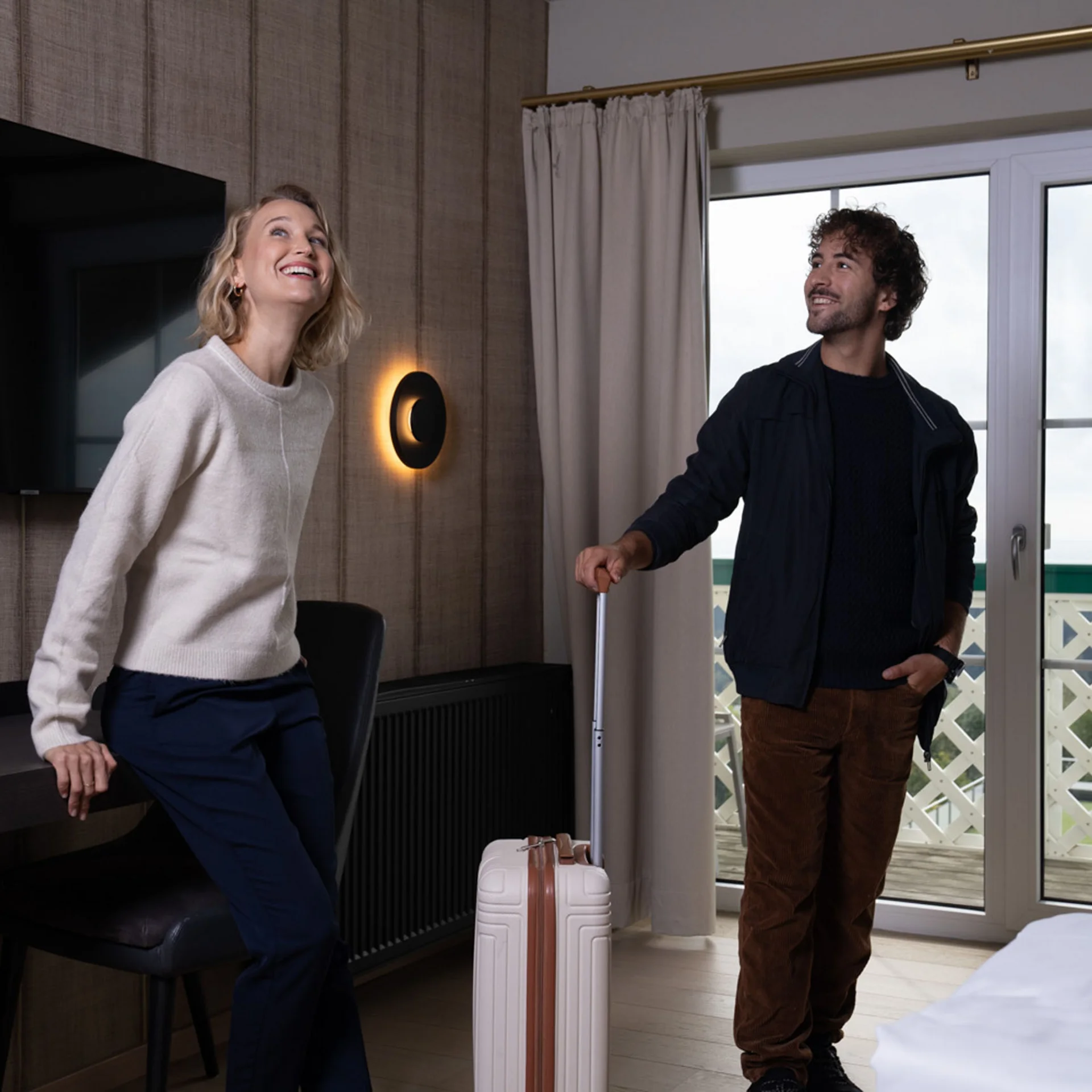 Zwei lächelnde Personen mit Koffer in einem modernen Hotelzimmer